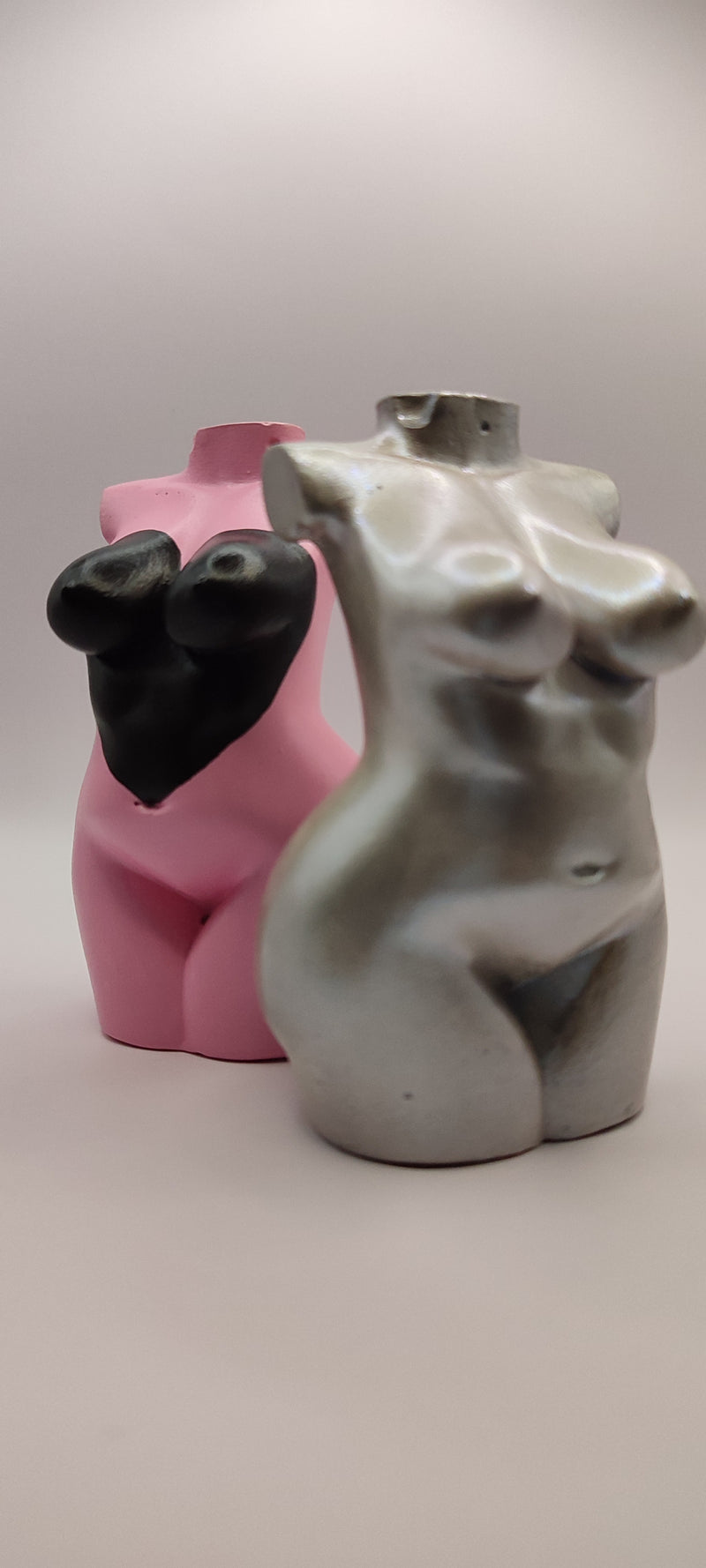 Two ceramic figurines, one pink and one gray, on a plain background